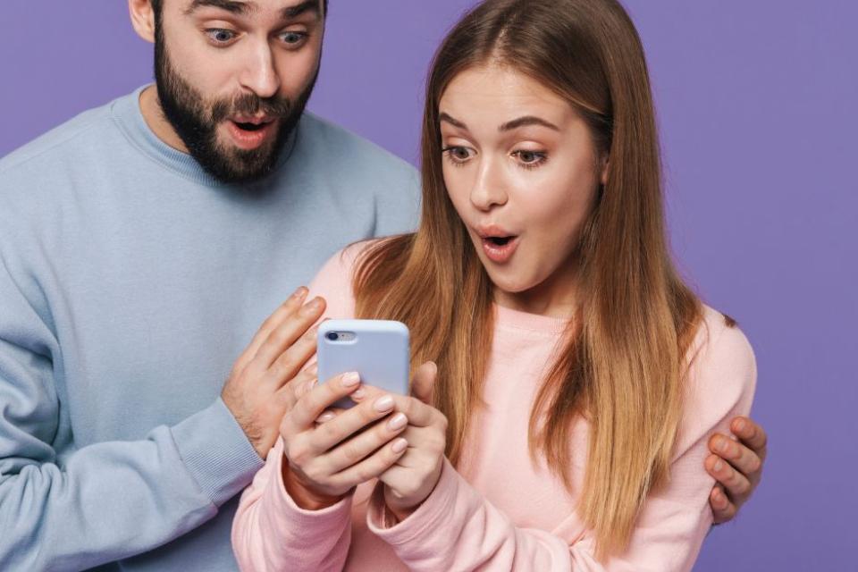 A man wearing a blue jumper and a women in a Pink Jumper holding a mobile phone