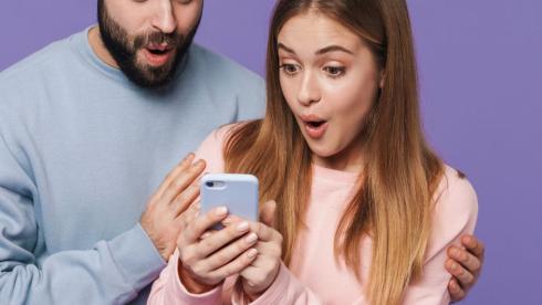 A man wearing a blue jumper and a women in a Pink Jumper holding a mobile phone