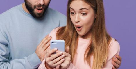 A man wearing a blue jumper and a women in a Pink Jumper holding a mobile phone